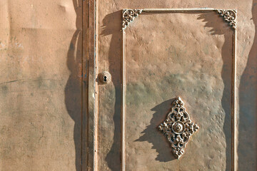 Close-up of an old iron door, with layers of beige and green paint and Baroque style decoration, Italy
