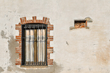 Close-up of the facade of an old building, with a brick framed window, closed by a wrought iron grate, Piedmont, Italy