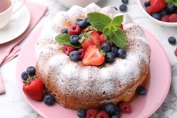 Tasty Bundt cake with powdered sugar and berries on white marble table, closeup