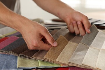 Man choosing fabric among different samples indoors, closeup