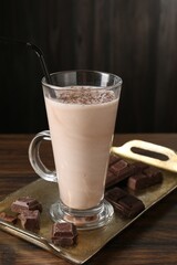Tasty milkshake in glass and pieces of chocolate on wooden table, closeup