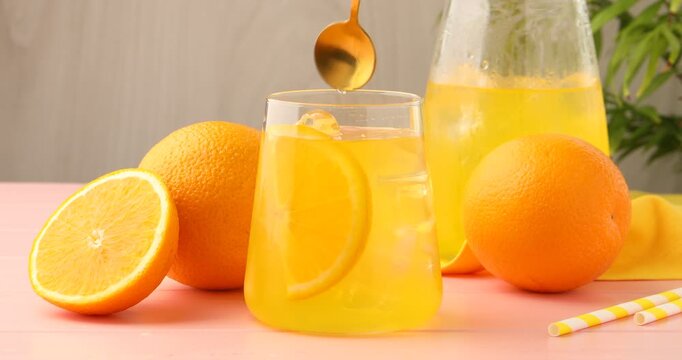 Woman stirring and putting straw into refreshing soda with orange slice and ice cubes at pink wooden table, closeup