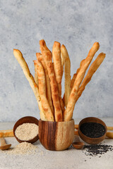 Wooden bowl with tasty Italian Grissini and sesame seeds on light background