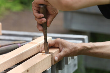 ノミで材木を削る男性