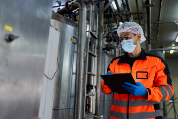 Workers in safety gear inside a factory are checking equipment and machinery to store chemicals and...