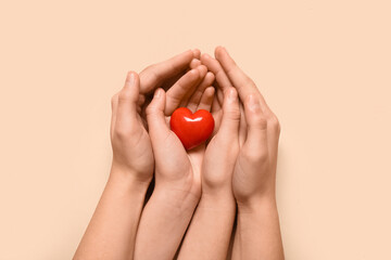 Hands of woman and child with red heart on beige background