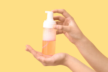 Female hands with bottle of cosmetic product on yellow background