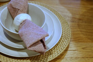 Prato branco com guardanapo de tecido rosa dobrado e talher, em mesa posta para refei&ccedil;&atilde;o elegante / White plate with folded pink cloth napkin and cutlery on set table for elegant dining