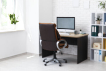 Interior of office with workplace, brown armchair, modern computer and shelving unit, blurred view