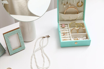 Box with stylish different jewelry, mirror and photo frame on table, closeup