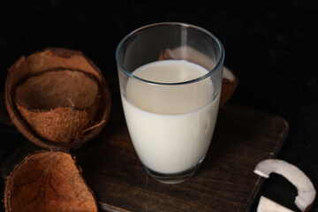Wooden tray and glass of tasty fresh coconut milk on black background, closeup