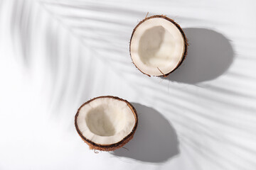Halves of fresh coconuts and shadow of palm leaf on white background
