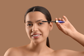 Fototapeta premium Pretty young woman applying mascara on beige background