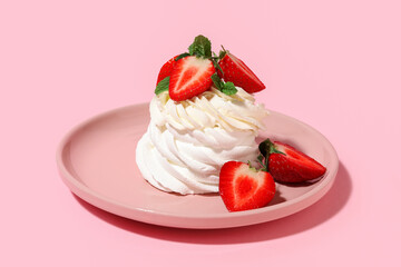 Plate of sweet Pavlova cake with fresh strawberries and mint on pink background