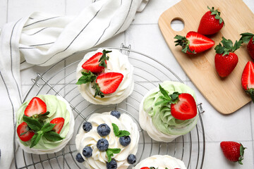 Stand of sweet Pavlova cakes with fresh berries and mint on white tile background