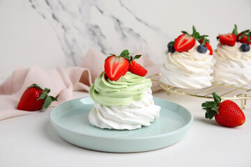 Plate and stand of sweet Pavlova cakes with fresh berries on white background
