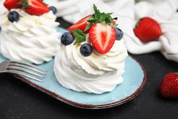 Plate of sweet Pavlova cakes with fresh berries and mint on black background