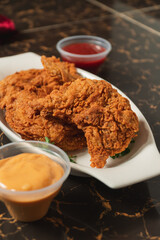 Close-up of fried chicken on a plate with sauces.