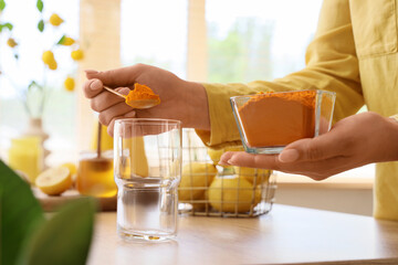 Woman making turmeric drink at table in kitchen, closeup