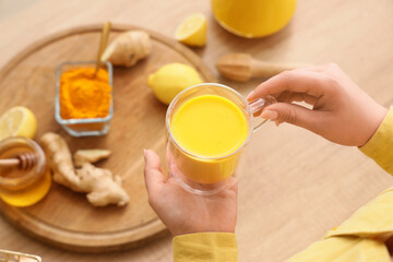 Woman with turmeric drink at table, closeup
