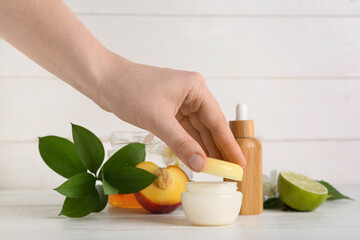 Female hand with natural cosmetic products on white wooden background