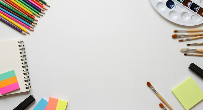 Flat lay of colorful art and craft supplies with colored pencils, paints, and a notebook on a white background with copy space