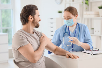 Fototapeta premium Young man receiving vaccine from doctor at table in clinic