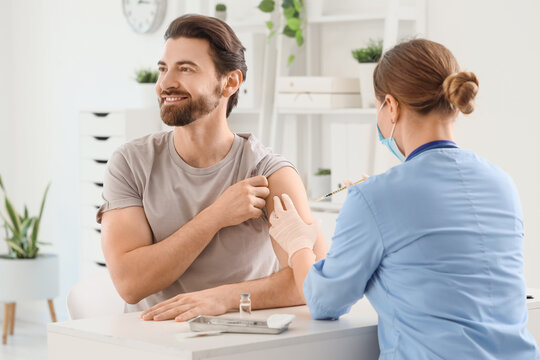 Young man receiving vaccine from doctor at table in clinic