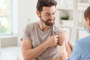 Young man with doctor applying medical patch after vaccination in clinic