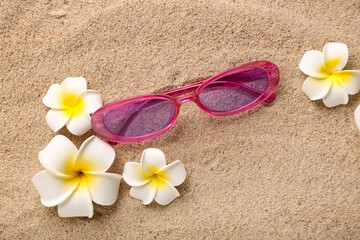 Plumeria flowers with pink sunglasses on sand