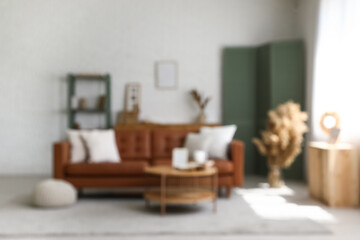 Blurred view of light living room with brown sofa, table and folding screen