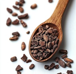 Obraz premium close-up view of a wooden spoon filled with cacao nibs scattered on a white surface, highlighting natural brown tones and textured chunks of raw cacao
