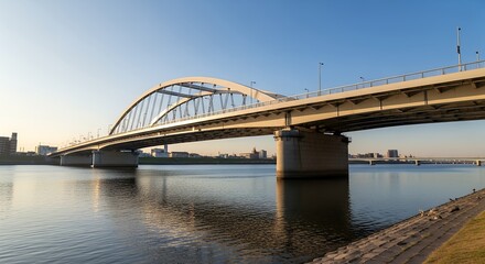 Fototapeta premium Modern Arched Bridge Spanning a Wide River at Sunset with City Skyline in Distance