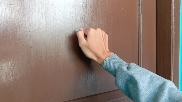 The hand of a young man knocking on a brown door is perfect for businesses related to housing, household appliances, or social activities