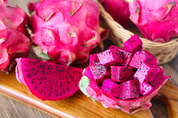Closeup of a vibrant arrangement of fresh dragon fruit, showing a whole fruit, a slice, and cubes of the flesh served in a bowl made from its own fruit skin.