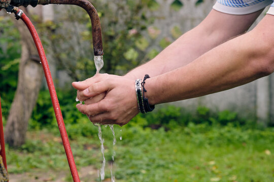 Hands under running water from an outdoor faucet in a green garden during a sunny day