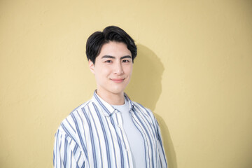 A man wearing a casual shirt with a smiling expression, looking at the camera against a yellow...