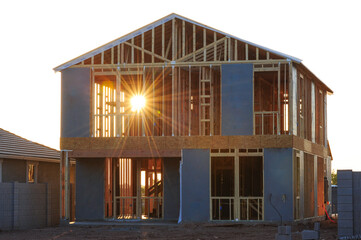 Obraz premium Two-story house under construction with exposed wooden framing and sheathing panels, captured at sunrise during the structural phase of residential building in a suburban housing development