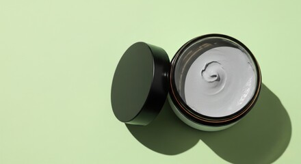 Top view of a cosmetic clay mask in an open jar on a green background