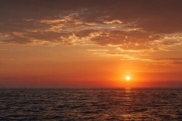 Sunset over a tranquil ocean.  Warm hues of orange and red paint the sky as the sun dips below the horizon, casting a gentle glow on the still ocean.  Soft, blurred clouds drift across the vibrant sky