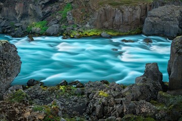 River with turquoise water flowing through rocky terrain surrounded by lush greenery in Iceland