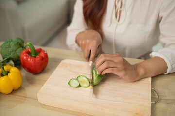 Fresh Vegetable Preparation on Wooden Cutting Board with Sliced Cucumbers and Colorful Bell Peppers in Modern Kitchen Setting