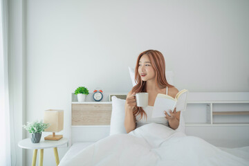 Young woman enjoying morning coffee and reading book in cozy bedroom with natural light and minimalist decor, relaxing weekend morning routine.