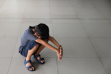 A Southeast Asian boy squatting on the floor in public area, bowing his head between his legs. Mental health issue concept.