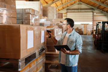Warehouse worker scanning barcodes on boxes using barcode scanner and tablet