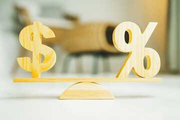 Wooden symbols of a dollar and a percentage sign balanced on a seesaw, representing interest rates, financial balance, and economic decisions.