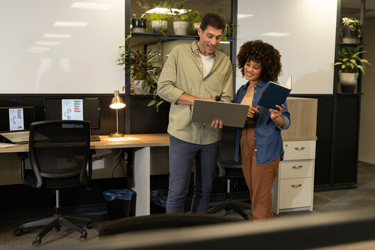 Collaborating Diverse coworkers discussing project at open-plan office, with laptop and notebook