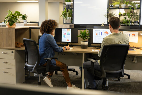 Collaborating Diverse coworkers analyzing charts in open-plan office, with potted plants
