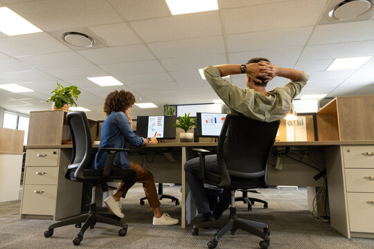 Diverse coworkers collaborating at open-plan office desks, with monitors showing charts and plants
