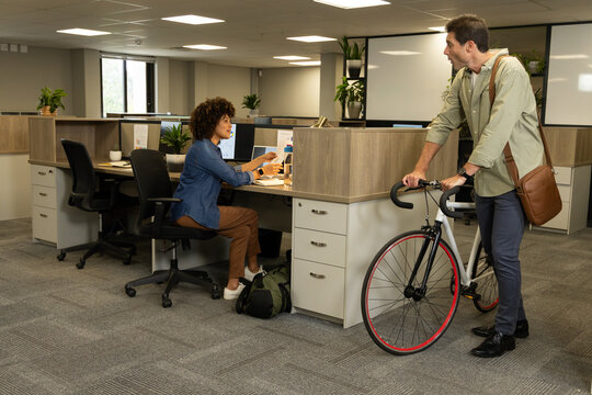 Collaborating Diverse coworkers sitting and standing in open-plan office, with bicycle and plants